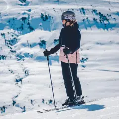 Narciarka w kasku i goglach stoi na stoku narciarskim z kijkami.