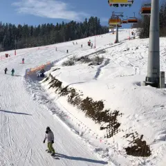 Narciarze i snowboardziści na ośnieżonym stoku z wyciągiem krzesełkowym w tle.
