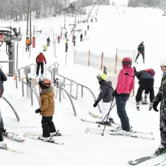 Ludzie w strojach narciarskich stoją w kolejce do wyciągu narciarskiego na ośnieżonym stoku.