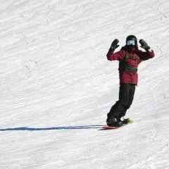 Snowboardzista w czerwonej kurtce z rękami w górze na ośnieżonym stoku.