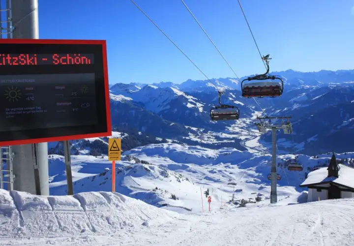 Zimowy krajobraz górski z wyciągiem krzesełkowym i tablicą informacyjną o pogodzie.