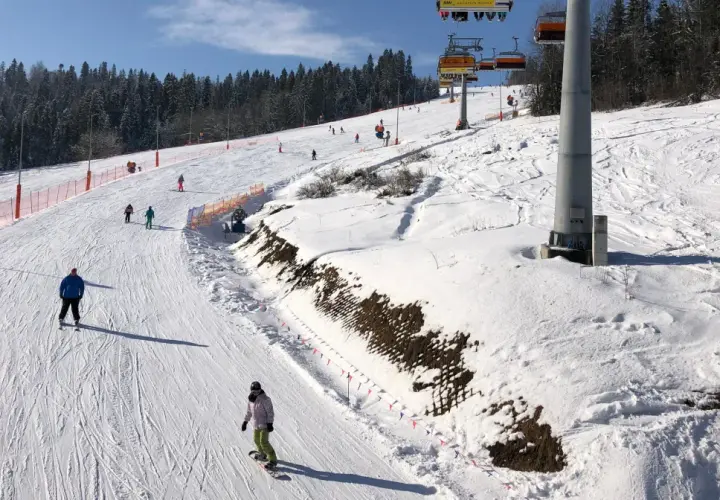 Narciarze i snowboardziści na ośnieżonym stoku z wyciągiem krzesełkowym w tle.