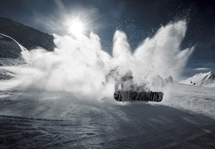 Snowboardzista wykonujący obrót 360 stopni, wzbijając chmurę śniegu.
