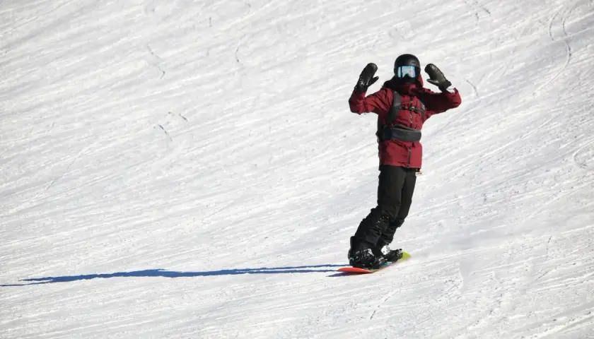 Snowboardzista w czerwonej kurtce z rękami w górze na ośnieżonym stoku.