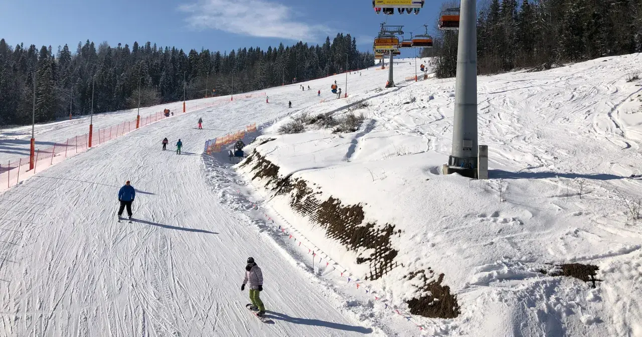 Narciarze i snowboardziści na ośnieżonym stoku z wyciągiem krzesełkowym w tle.