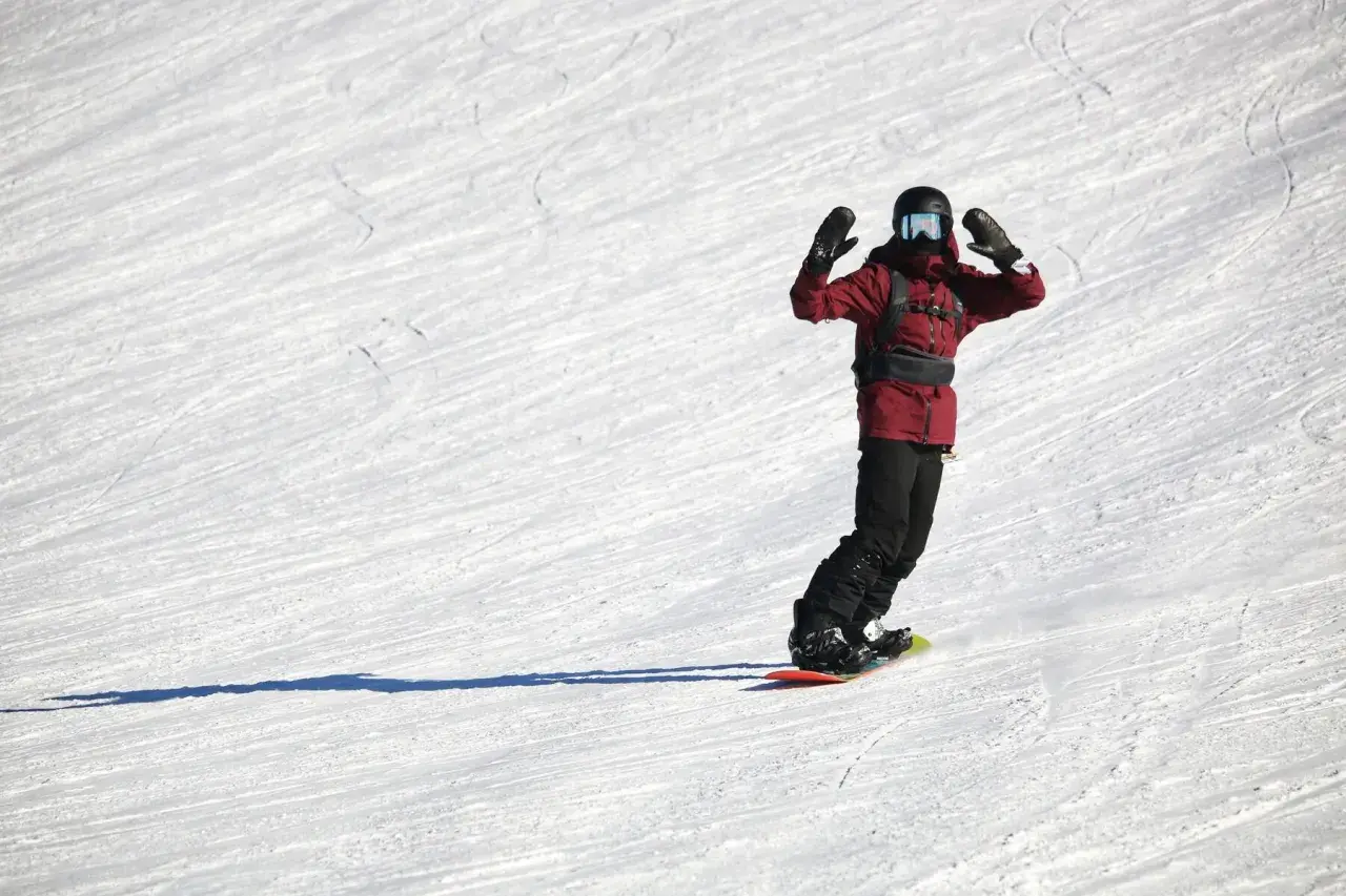 Snowboardzista w czerwonej kurtce z rękami w górze na ośnieżonym stoku.